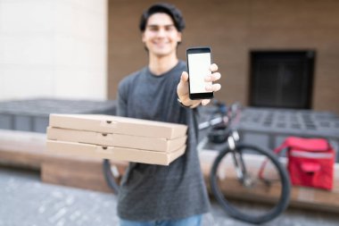 Pizza kutuları dağıtırken akıllı telefon gösteren teslimatçı.