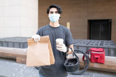 Paket ve tek kullanımlık kahve bardağı taşıyan yüz maskeli bir teslimatçı.