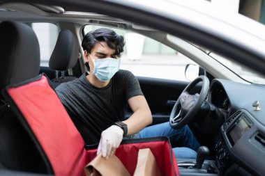 Latin maskeli genç teslimatçı arabada paket çıkartıyor.