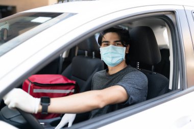 Araba kullanırken yüz maskesi takan genç teslimatçı.