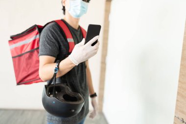 Kapıda beklerken akıllı telefon kullanan teslimatçının orta bölümü.