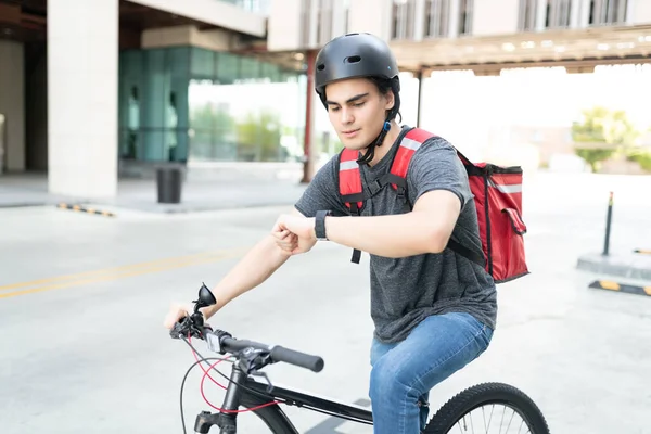 İspanyol kurye bisiklet sürerken kol saatini kontrol ediyor.