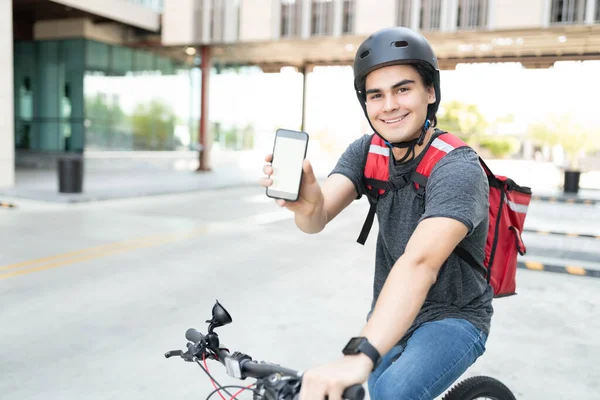 Retrato Homem Entrega Hispânico Sorridente Mostrando Smartphone Enquanto Sentado Bicicleta — Fotografia de Stock