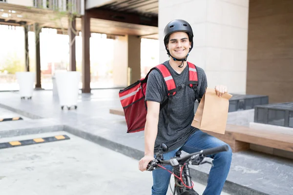 Confiante Jovem Entregador Segurando Parcela Enquanto Sentado Bicicleta — Fotografia de Stock