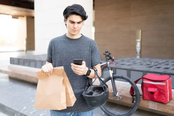 Young delivery man using app on smartphone while holding parcel