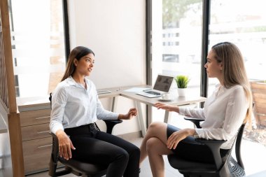 İki kadın iş ortağı ofis masasında yeni bir proje üzerinde tartışıyorlar.