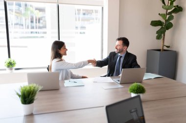 Ofis toplantısında gülümseyen işadamı iş arkadaşıyla tokalaşıyor.
