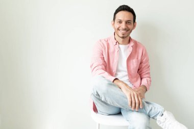 Güzel görünümlü genç bir adamın portresi. Sıradan giyinmiş ve bir sandalyede oturuyor. Bir sürü fotokopi alanı var.