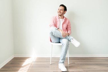 Sandalyede rahatlayan bir adamın tam boy görüntüsü ve başka bir yere bakıp gülümsemesi.