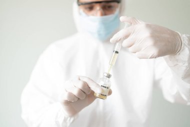 Koruyucu giysi giyen erkek doktor ve şırıngaya COVID19 aşısı hazırlıyor.