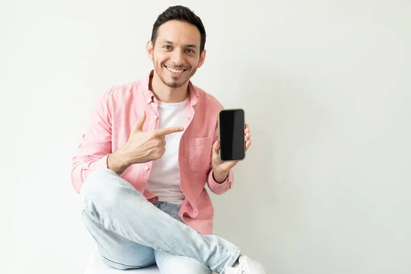 Sıradan Giyinmiş Stüdyodaki Akıllı Telefon Ekranını Işaret Eden Mutlu Genç — Stok fotoğraf