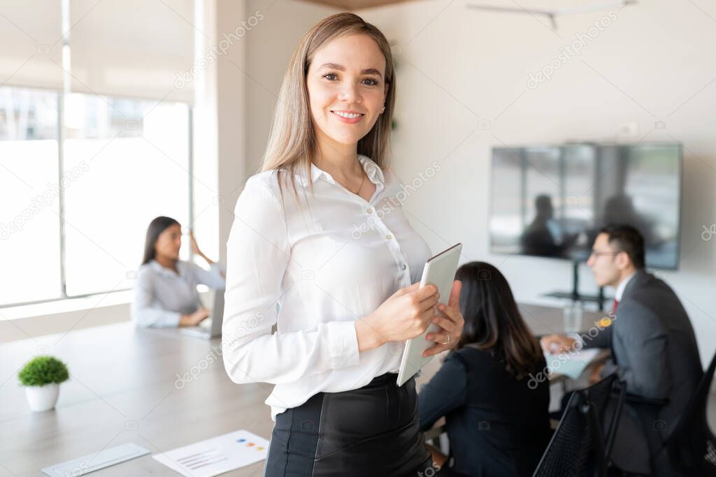 Portrait of a confident young caucasian businesswoman with a digital tablet standing in meeting room