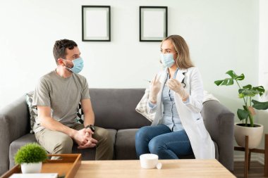 Doktor ve hasta yüz maskesi takarken doktor aşının olası ikincil etkilerinden bahseder.