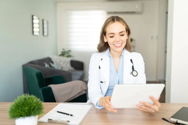 귀여운 여의사가 집에서 일하면서 웃으면서 태블릿 컴퓨터로 환자와 이야기하는 — 스톡 사진