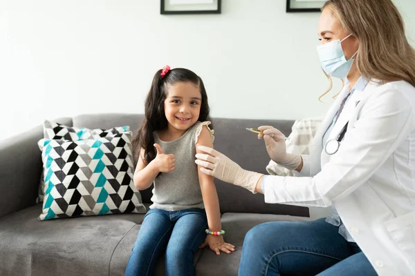 一个漂亮的小女孩竖起大拇指准备注射疫苗的画像 坐在一个拿着注射器的医生旁边 — 图库照片