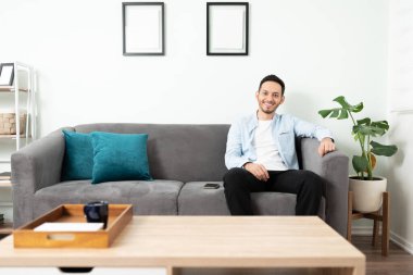 Genç latin adam yeni evindeki bir kanepede oturup dinleniyor.