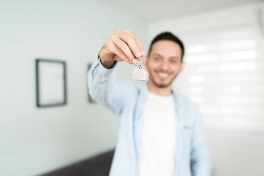 Çekici genç bir adam yeni evinin anahtarlarını tutuyor ve gülümsüyor. Anahtarlara odaklan..