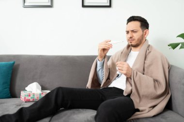 Yakışıklı bir adam termometreye bakarken kanepede dinlenirken midesi bulanıyor.