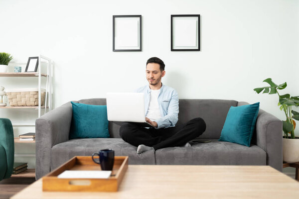 Handsome man in his 30s doing home office and sitting on his living room couch