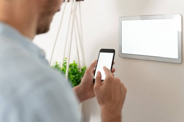 Akıllı telefonunu akıllı ev sistemine bağlayan genç bir adamın yakın çekimi.