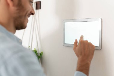 Akıllı ev aletlerini kontrol etmek için dokunmatik ekran kullanan genç bir adamın yakın çekimi.