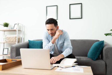 30 'lu yaşlarda İspanyol bir adam evinden laptopuyla uğraşırken meşgul ve odaklanmış görünüyor.
