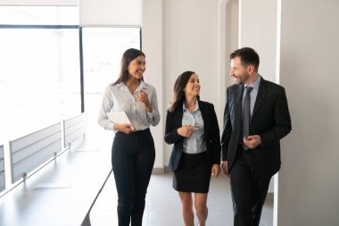 Üç profesyonel iş adamı birlikte yürüyor ve ofiste iş tartışıyorlar.