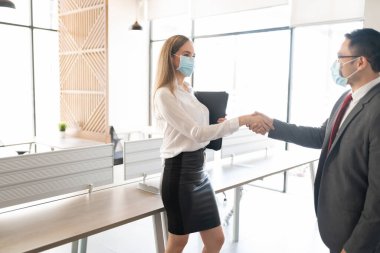 Ofiste el sıkışan koruyucu maskeler takan iki iş ortağı.