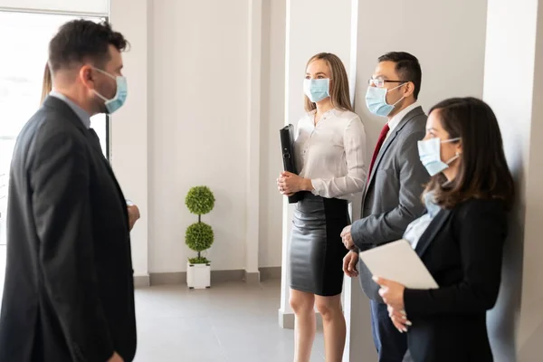戴面具的商人与站在办公室很远的团队交谈 在科罗那病毒爆发期间站在一起 — 图库照片