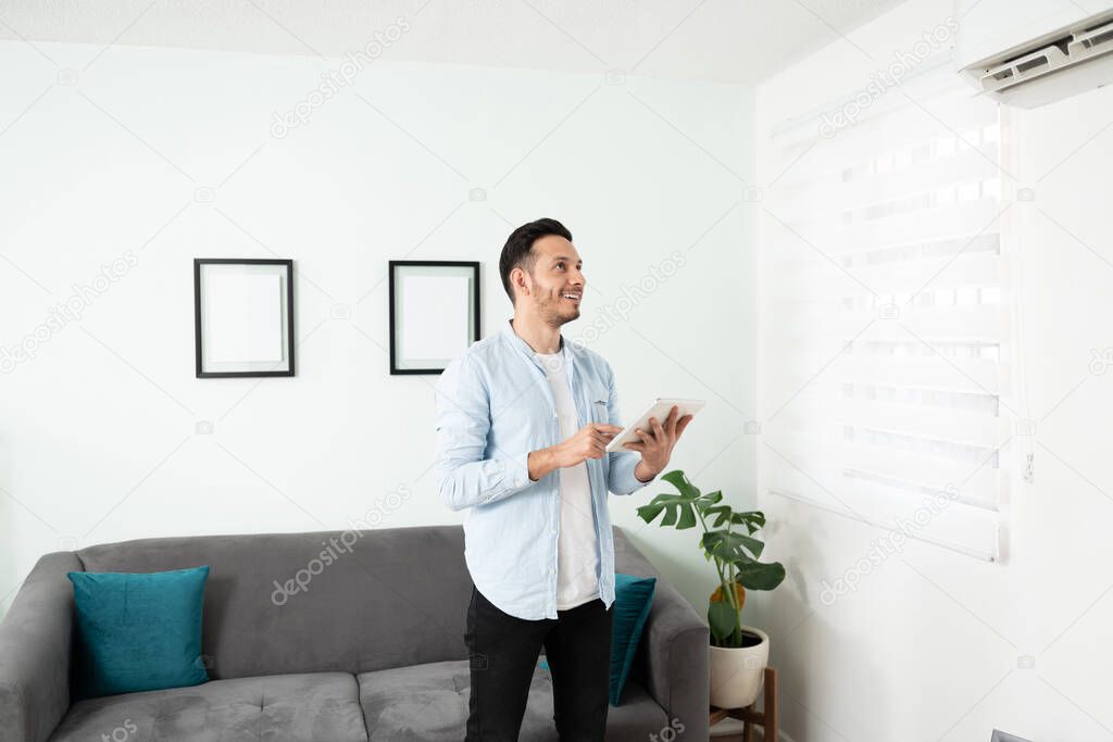 Handsome man in his 30s turning on the AC unit with a tablet computer in his smart home