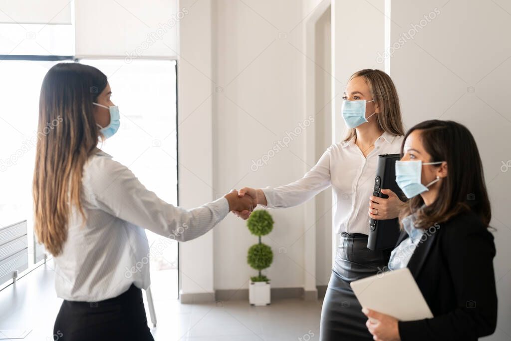 Businesspeople wearing protective face masks shaking hands in office during pandemic