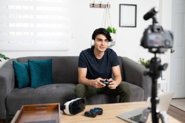 Video blogger and influencer wearing headphones and reviewing video games on camera for some of his viewers clipart