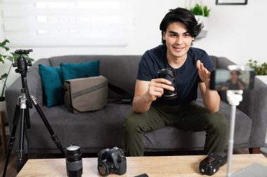 Genç adam ve video blogcusu bazı fotoğraf malzemelerini inceliyor ve sosyal medya izleyicilerine yeni bir lens aldığını söylüyor.