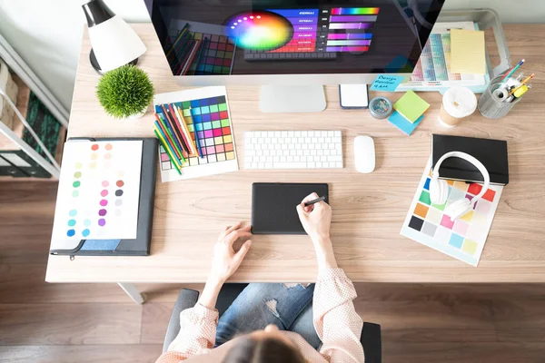一个女人用图形平板电脑在她的工作空间里用许多彩色调色板和石板做一些设计工作的头像 — 图库照片