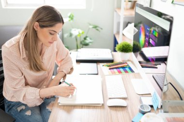 Ofisinde çalışırken bir not defterine çizim yapan çekici bir kadın çizer.