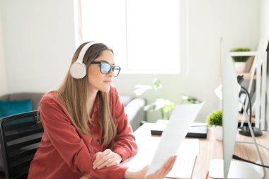 Güzel beyaz esmer, kulaklıkla müzik dinlerken bazı belgeler okuyor ve içerik yazıyor.