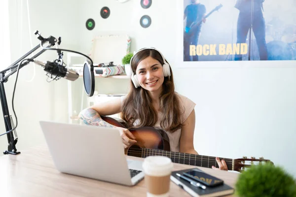ラテン系の女性ミュージシャンがギターを弾き 彼女のオンラインショーのために曲を録音する姿 — ストック写真