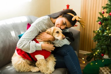 İspanyol kadın ve köpek anne ren geyiği boynuzları takıyor Noel ağacının yanındaki koltukta otururken köpeğine sarılıyorlar.