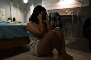 İlişkiden sonra kalp kırıklığı ve yalnızlık yaşayan üzgün Latin bir kadın. Yatak odasında tek başına, elleri ve ayakları üzerinde oturuyor.
