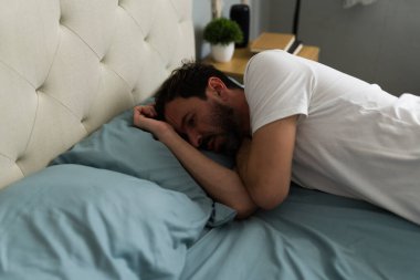 Üzgün bir adam, üzgün bir şekilde yatağa uzanmış, zor bir ilişkiden sonra yalnızlık ve depresyonla boğuşuyor, umutsuzlukla sarılmış.