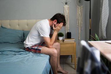 Ayrıldıktan sonra yatakta oturan üzgün adam, kafasını elinde tutuyor ve depresyondan acı çekiyor.