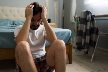 Endişeli bir adam, ayrılık sonrası üzüntü ve yalnızlık yaşıyor. Yatak odasında elleri bağlı oturuyor.