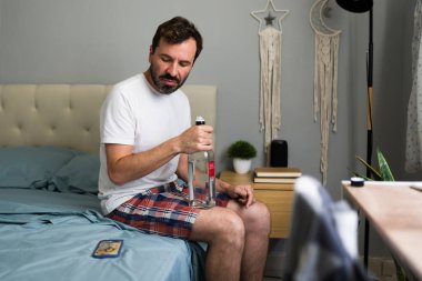 Mutsuz bir adam yatakta oturmuş, ayrılıktan sonra elinde alkol şişesiyle depresyon ve yalnızlıktan muzdarip.