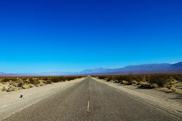 Classic panorama view of an endless straight road running through the barren scenery of the American Southwest with extreme heat haze on a beautiful sunny day with blue sky in summer.