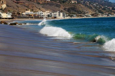 Güzel kumlu sahilde kalp şeklinde kaya, bulutlu gökyüzü, güneş ışınları, yansımalar ve dalgalar güneş doğduktan hemen sonra.