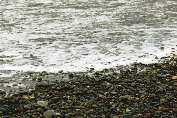 Piedras de guijarro en la playa, las olas onduladas del mar con espuma. — Foto de Stock