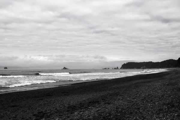 Cailloux sur une plage de sable, pierres mouillées brillantes et vagues. — Photo