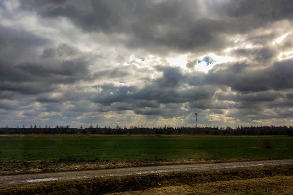 Green field against the dark sky, the sun through the clouds.