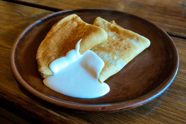 Pancakes on a plate with sour cream. Traditional for the Russian pancake week. Dark background. — Stock Photo, Image