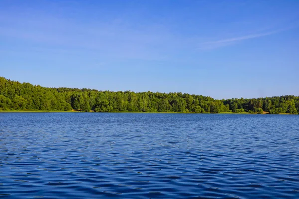 Θέα σε μια γαλάζια λίμνη ή ποτάμι σε μια ηλιόλουστη μέρα με φόντο το γαλάζιο του ουρανού και το πράσινο δάσος. — Φωτογραφία Αρχείου